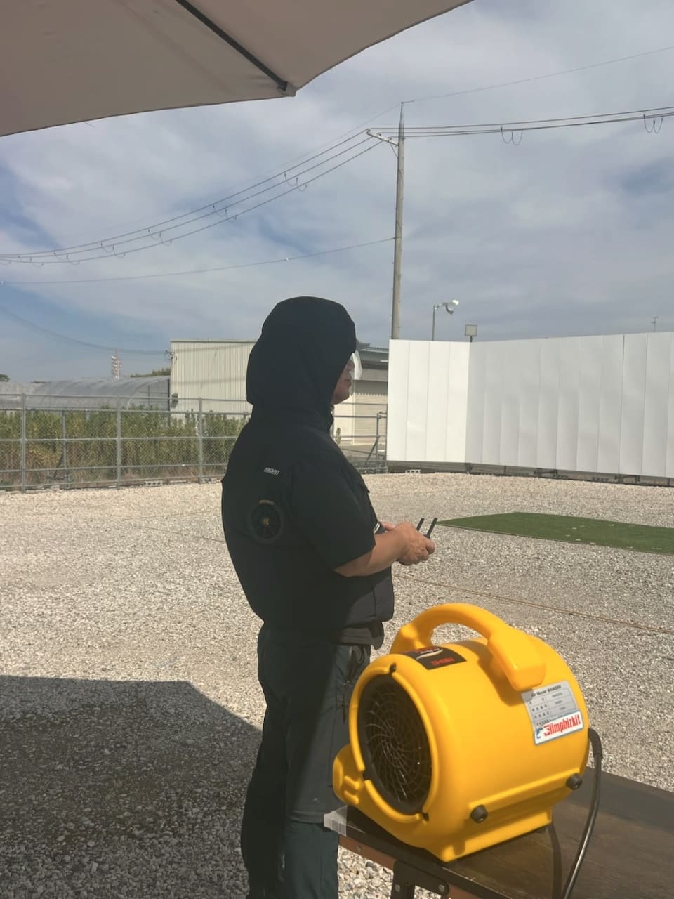 大型送風機のそばでファン付き空調服を着てドローンを操縦する様子